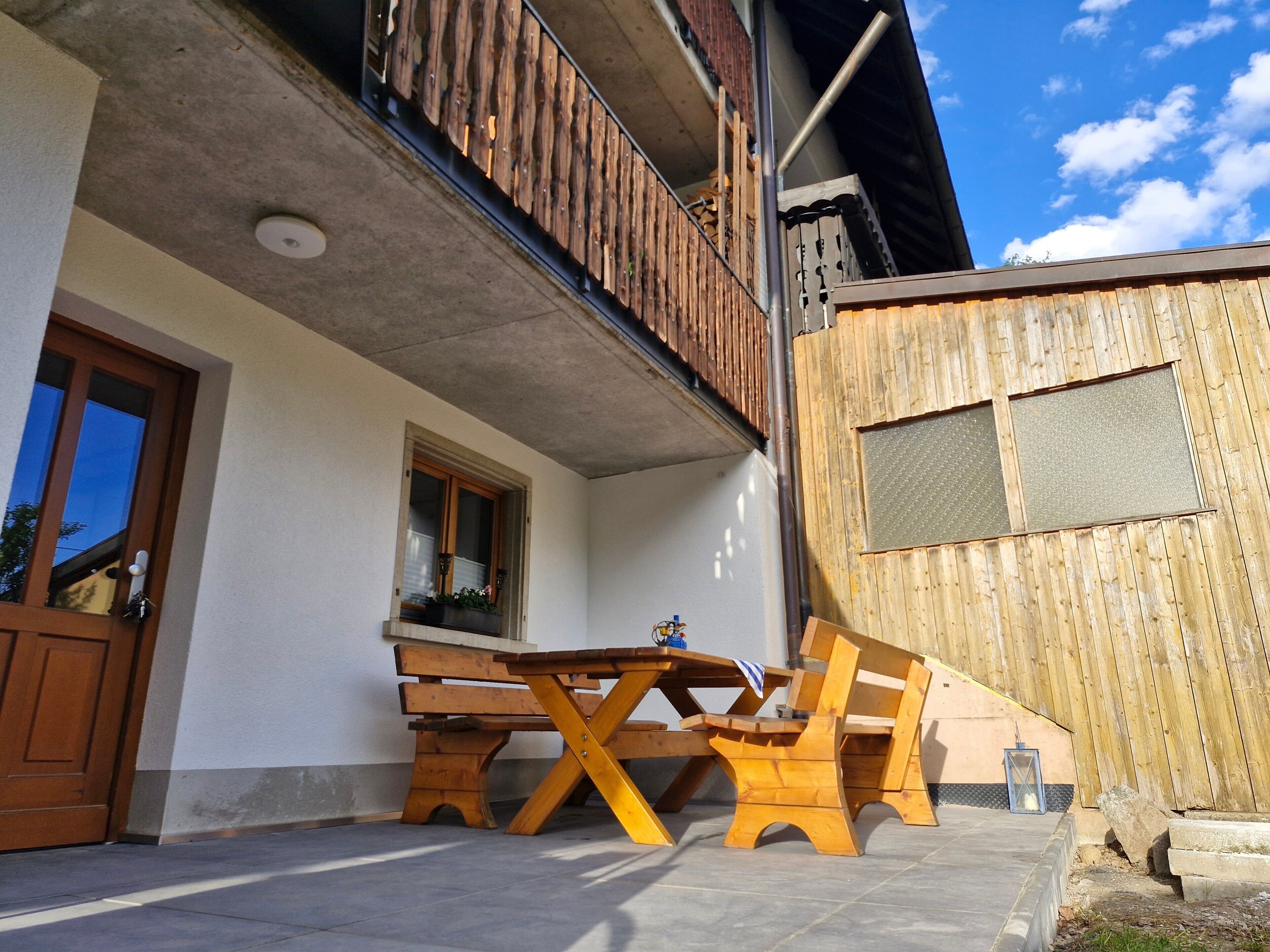 Eine Terrasse mit Holzmöbeln, ein Fenster mit Aussicht und ein Balkon.