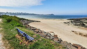 A beach with a bench, rocky shoreline, and a distant cityscape. - 4 bedroom stunning home in Plouigneau (Plouigneau)