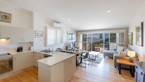 A modern kitchen with a central island, dining area with a table and chairs, and a living room with a sofa and a coffee table.