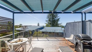 A covered outdoor deck with a grill, seating area, and a view of the ocean.