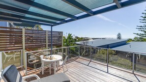 Una terrazza esterna coperta con tavolo e sedie, affacciata su una zona residenziale e l'oceano.