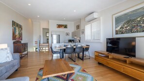 A modern living room with a wooden coffee table, a gray sofa, a TV on a wooden stand, and a dining area with a table and chairs.