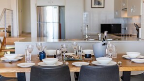 A dining area with a wooden table set for a meal, a kitchen in the background, and a modern design.