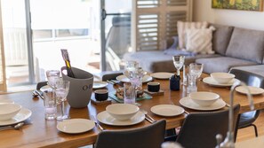 A dining table set with plates, glasses, and cutlery, with a bottle of champagne and a decorative bowl. - Angourie Blue 3 - Lifestyle Yamba (ANGOURIE)