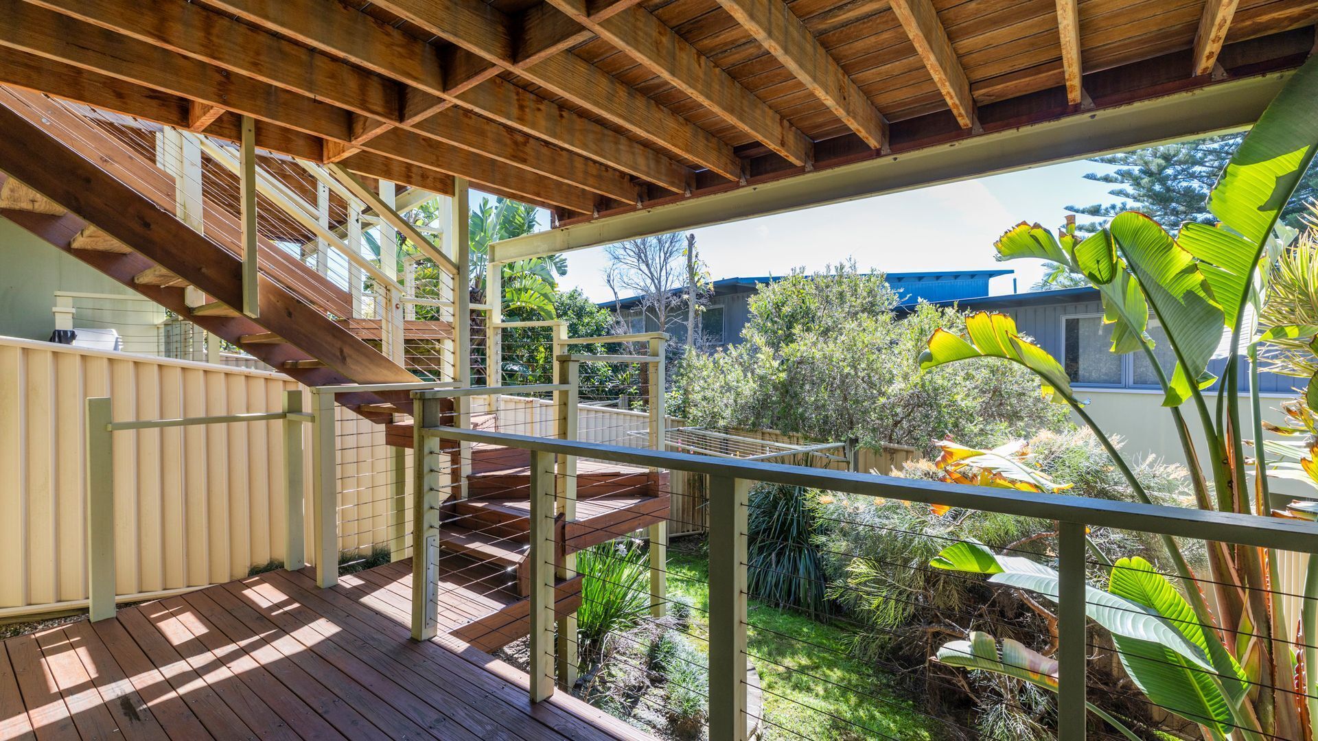 A wooden deck with a metal railing, a staircase, and a view of a garden with various plants.