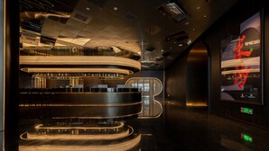 Et moderne barområde med en buet bar, flere siddepladser og et stort digitalt display på væggen.