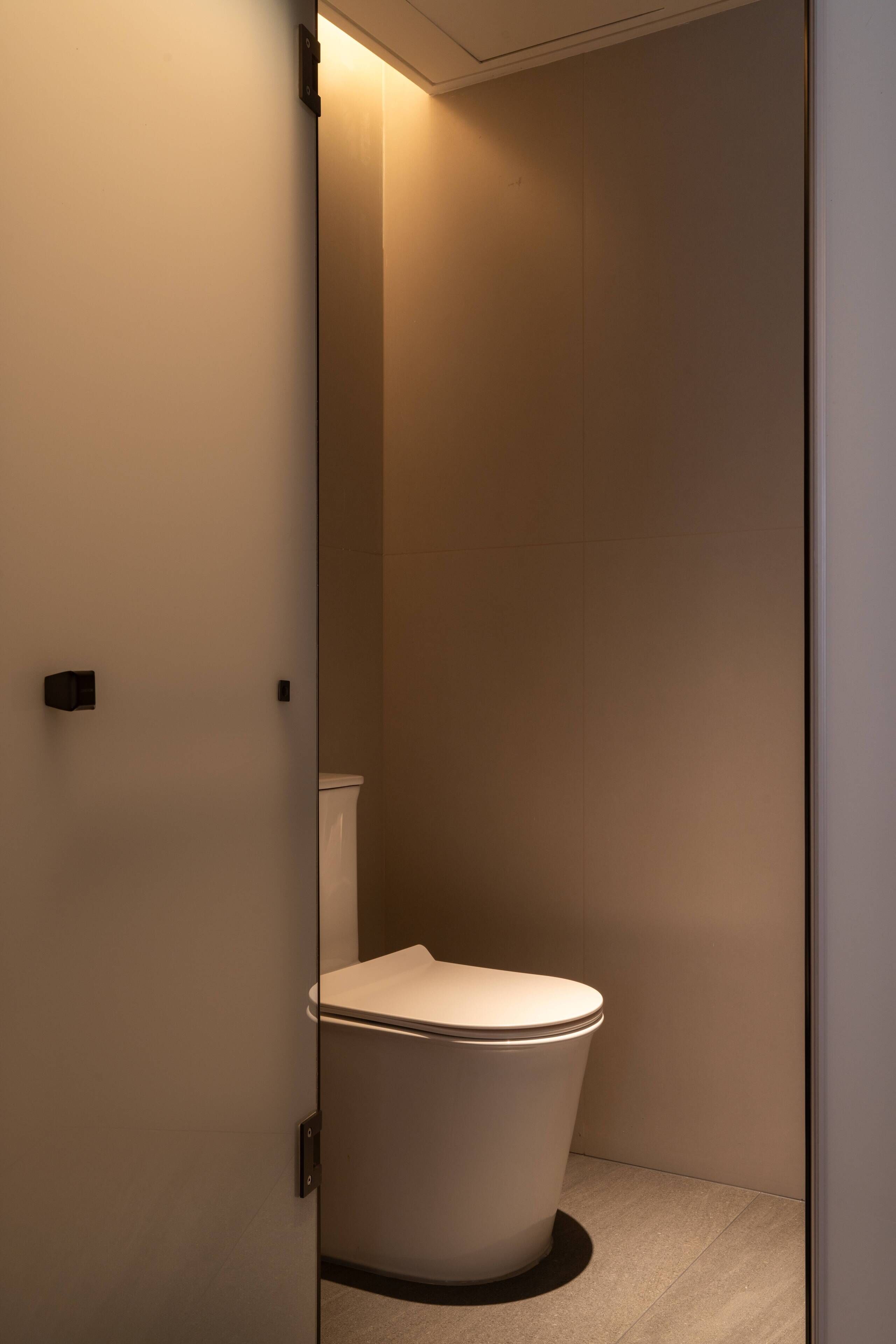 A modern bathroom with a toilet, a wall-mounted light, and a door.