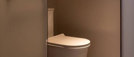 A modern bathroom with a toilet, a wall-mounted light, and a door.