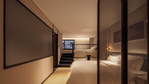 Et moderne hotelværelse med en stor seng, en mindre seng og et siddeområde. En trappe fører op til en etage ovenpå.
