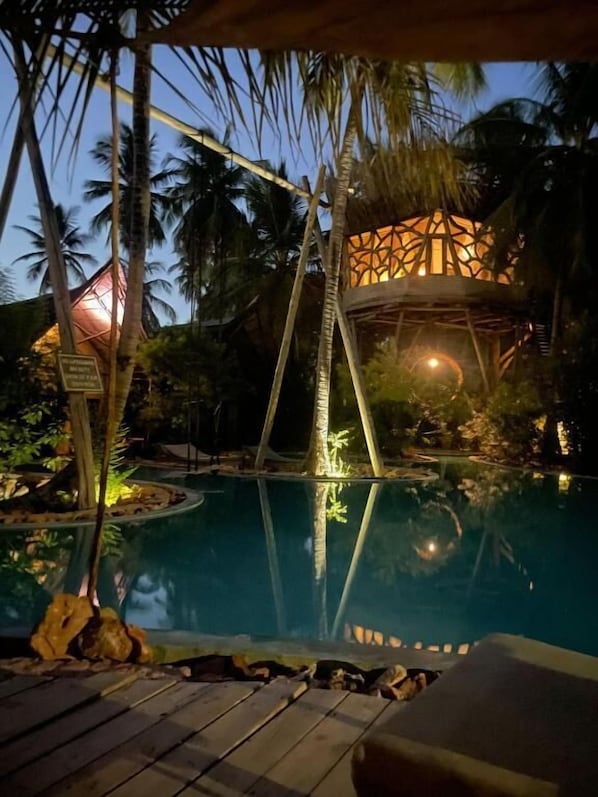 A pool area with a wooden deck, palm trees, and a building with a geometric facade. - The Nest Boutique Resort (Paje)