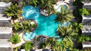 Oversigtsbillede af et resort med flere forbundne swimmingpools, omgivet af palmer og liggestole.