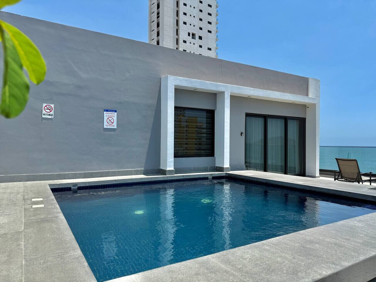 A swimming pool with a modern building in the background, a no smoking sign, and a view of the ocean.