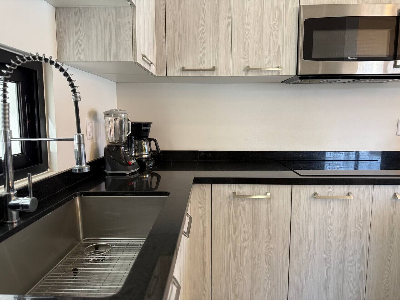 A modern kitchen with stainless steel appliances, a black countertop, and light wood cabinetry.
