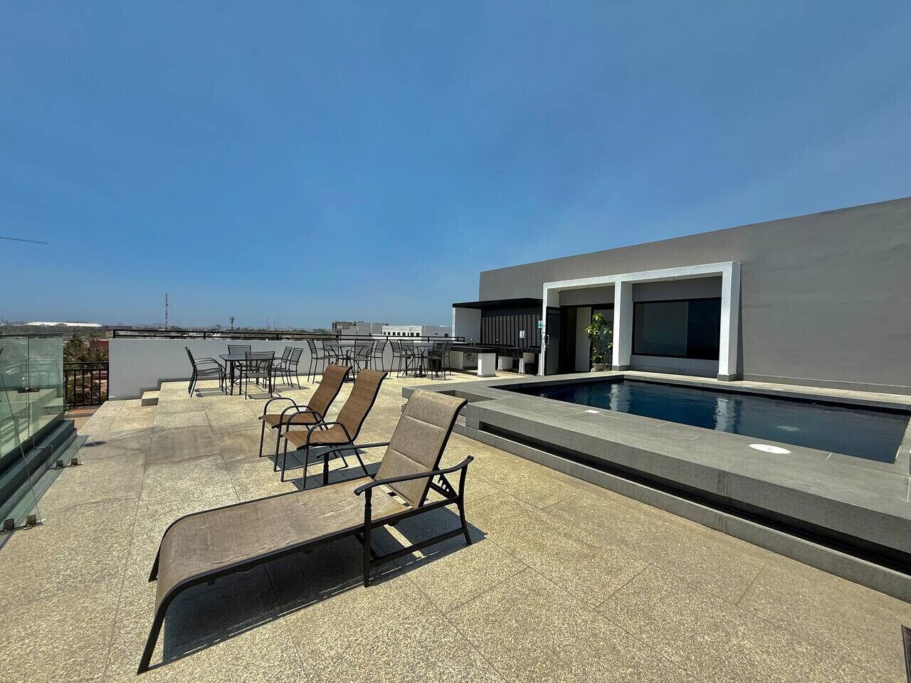 A rooftop terrace with a pool, lounge chairs, and a modern building.