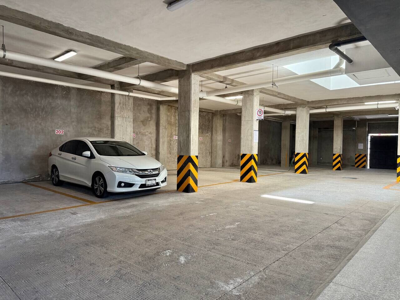 A parking garage with concrete pillars, a white car parked, and directional signs.