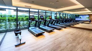 A gym with treadmills aligned against a wall with large windows overlooking a green area. - Address Dubai Opera 2BR Walk to Mall Burj Khalifa Opera (Dubai)