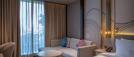 Una habitación de hotel moderna con sofá, sillón y una pequeña mesa redonda.
