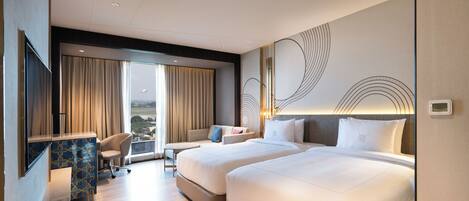 A hotel room with two beds, a desk, a chair, and a view of the airport.