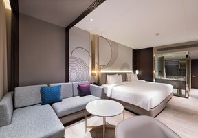 Una habitación de hotel moderna con sofá, cama, una pequeña mesa redonda y un espejo grande.