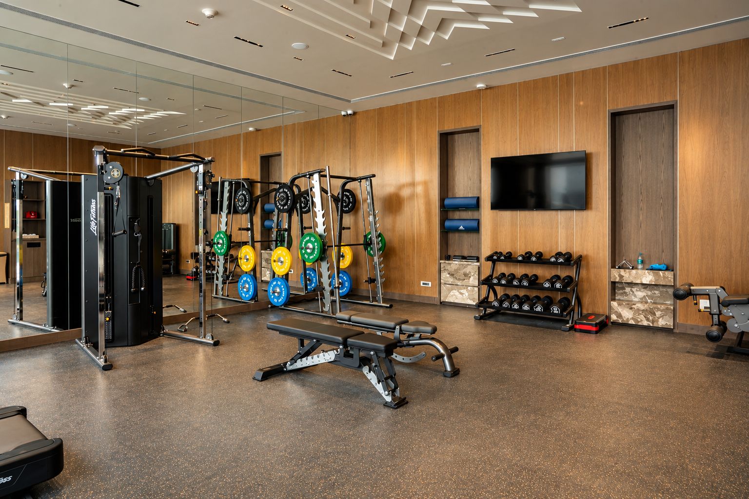 Ett gym med utrustning för styrketräning, en bänk och en tv på väggen.
