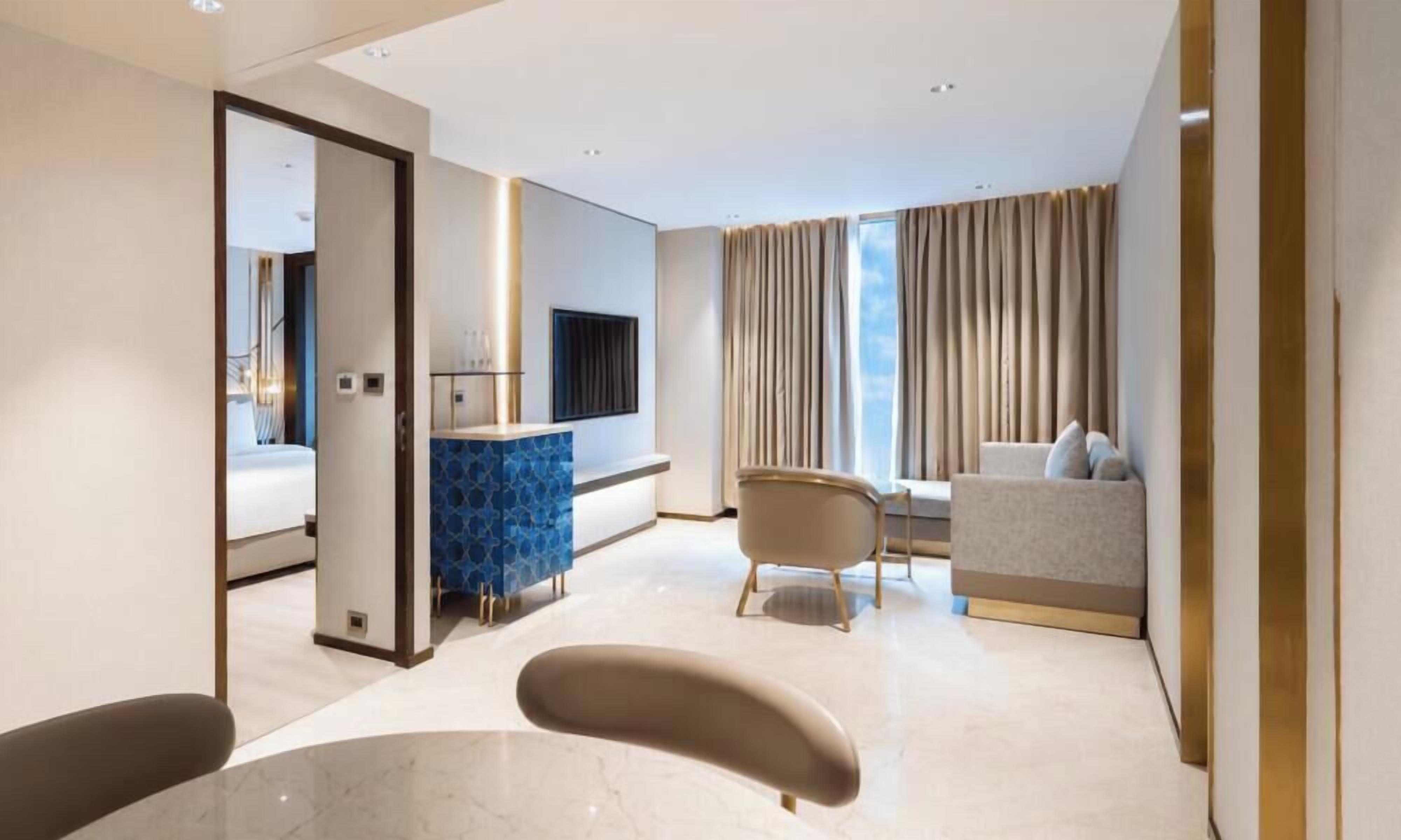 Habitación de hotel moderna con cama, zona de estar con sofá y sillones, una mesita y televisión.
