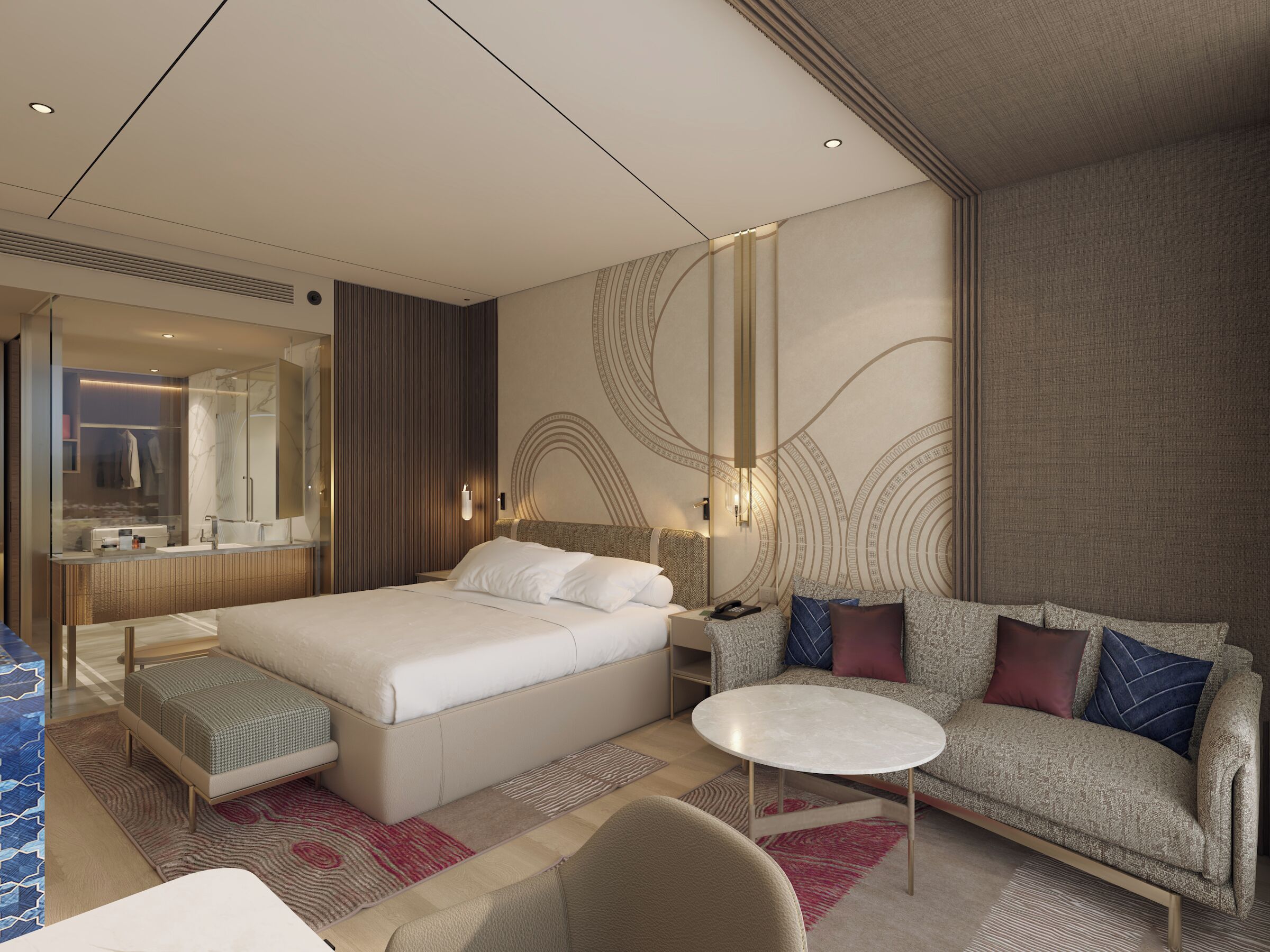 A modern hotel room with a large bed, a sofa, a small table, and a bathroom with a mirror and vanity.