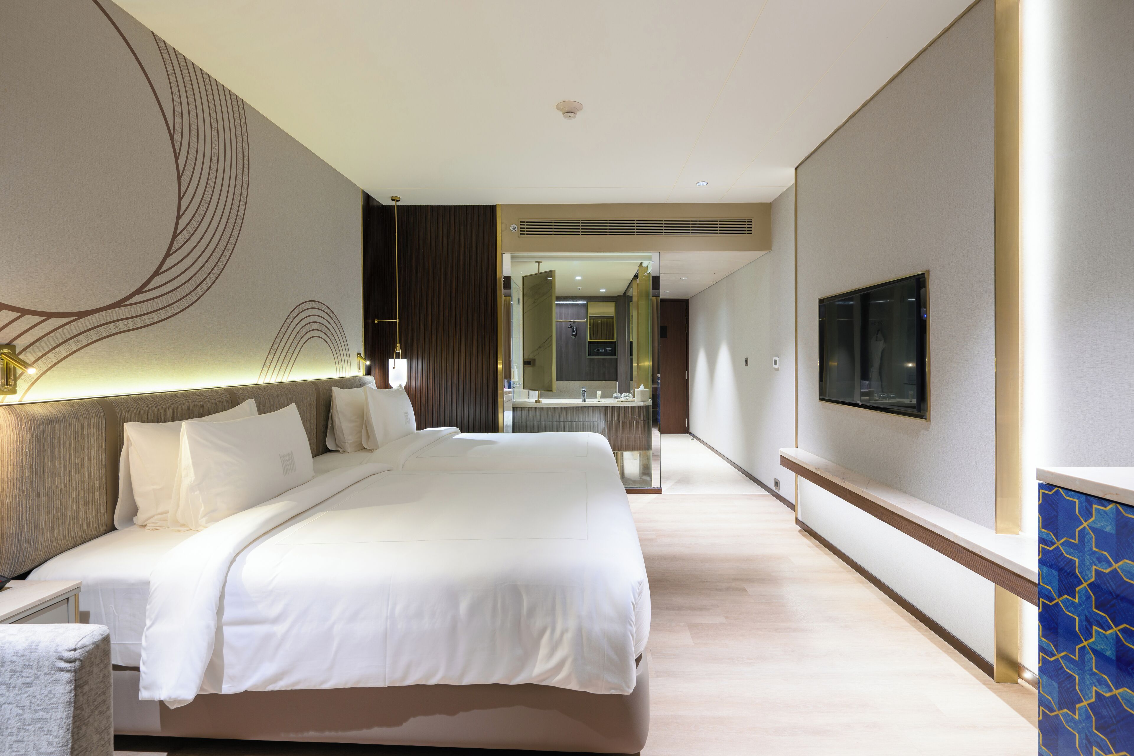 Una habitación de hotel moderna con una cama grande, televisor y baño con espejo y lavamanos.