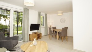 Un salon moderne doté d’un téléviseur à écran plat, d’une table basse en bois, d’un canapé, d’une table à manger avec des chaises et d’une porte-fenêtre coulissante donnant sur une terrasse.