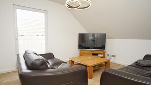 Ein modernes Wohnzimmer mit einem braunen Ledersofa, einem Holztisch und einem Flachbildfernseher auf einem Schrank.