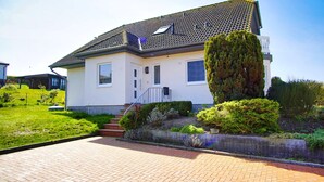 Ein modernes, zweistöckiges Haus mit Ziegeldach, einer kleinen Veranda und einem gepflegten Garten.