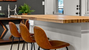 A modern kitchen with a wooden island, four wooden chairs, and a potted plant. - Modern Arvada Suite | Sauna & Games (Arvada)