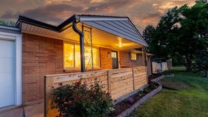A house with a brick exterior, a wooden fence, and a well-lit porch. - Modern Arvada Suite | Sauna & Games (Arvada)