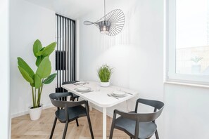 Un espace repas moderne avec une table blanche, des chaises noires, une plante en pot et un luminaire suspendu original.