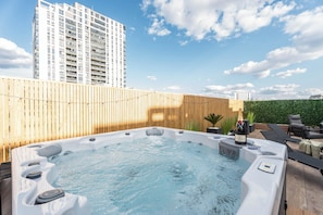 Un bain à remous avec une bouteille de champagne, entouré de chaises longues et d’une clôture en bois.
