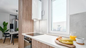 A modern kitchen with a white countertop, wooden cabinets, a built-in oven, and a window with a view of the outside. - Luxurious Brand New! Private Jacuzzi + Terrace + Parking (Warszawa)