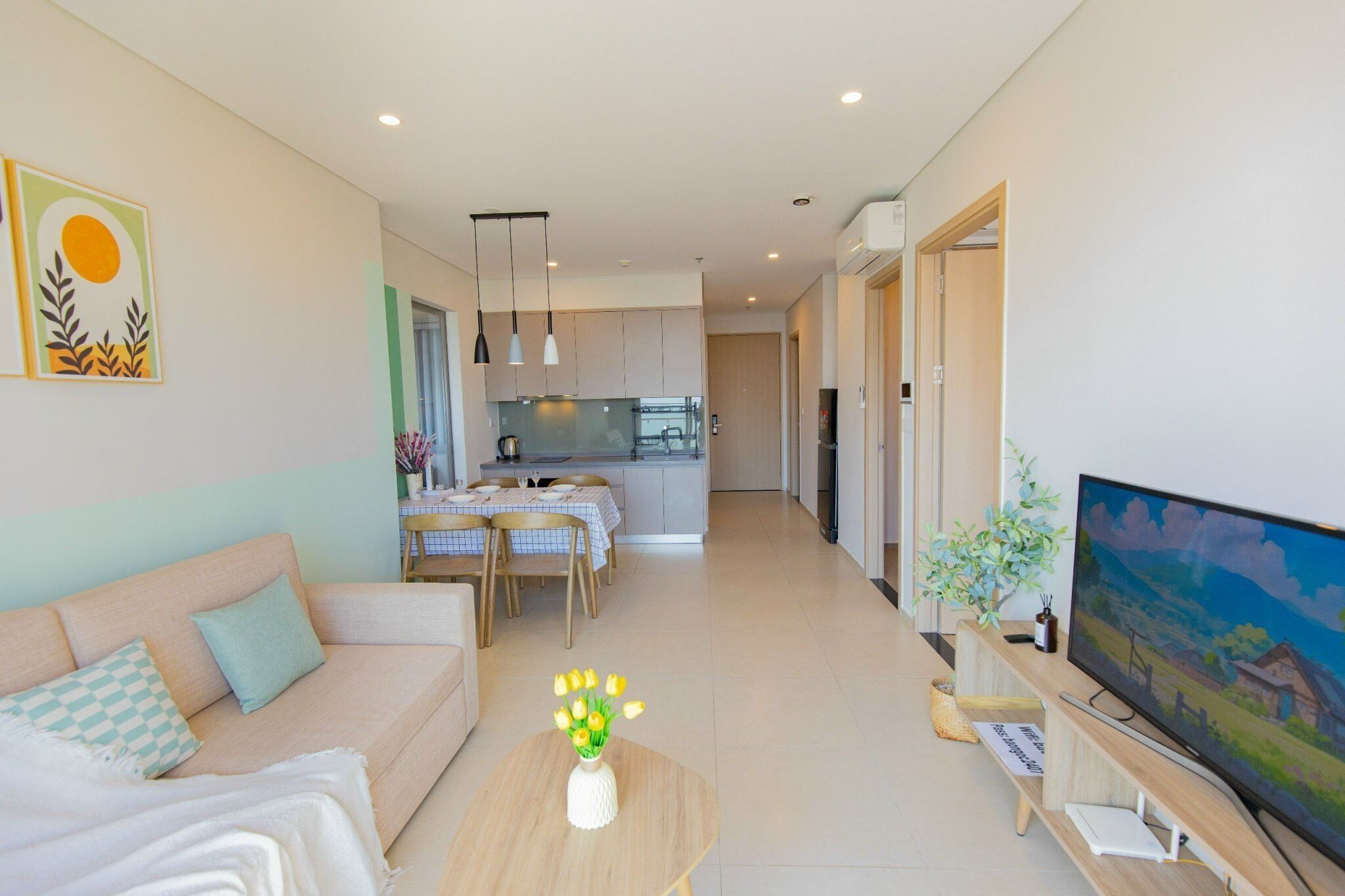 A modern living room with a sofa, a coffee table with flowers, a TV, and a kitchen in the background.