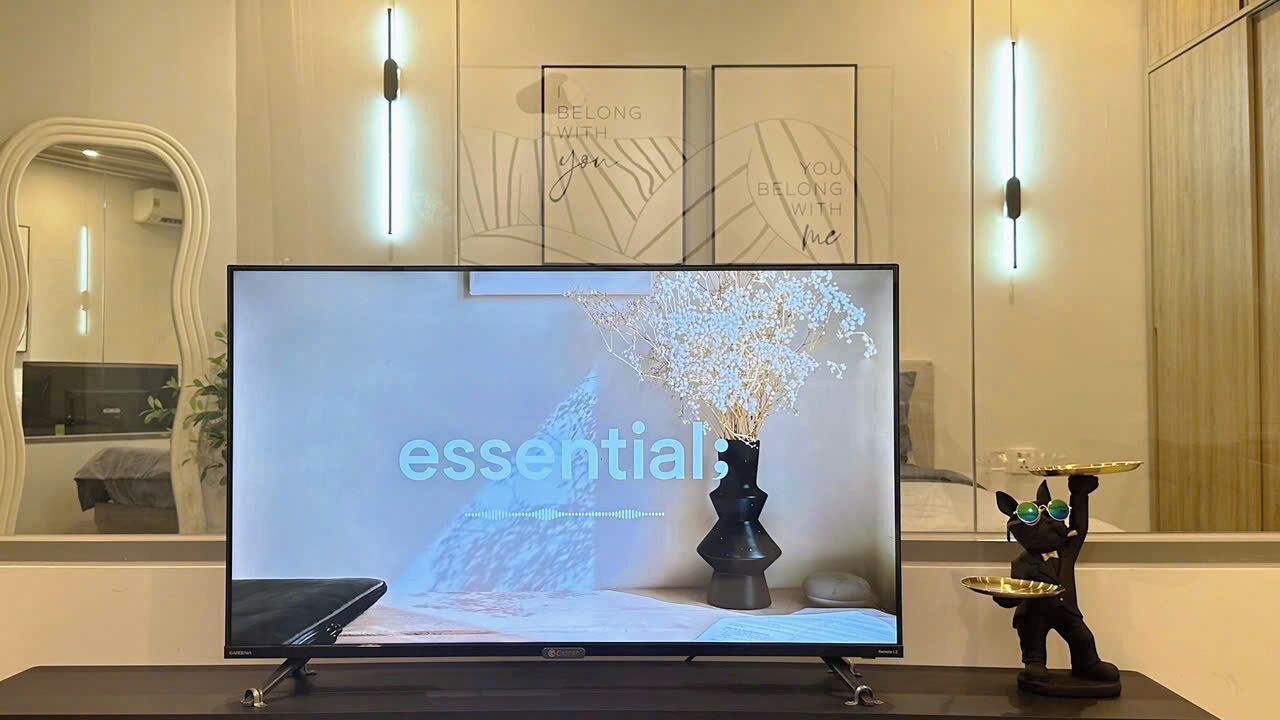 A flat-screen TV on a stand with a decorative vase and a figurine on the table.