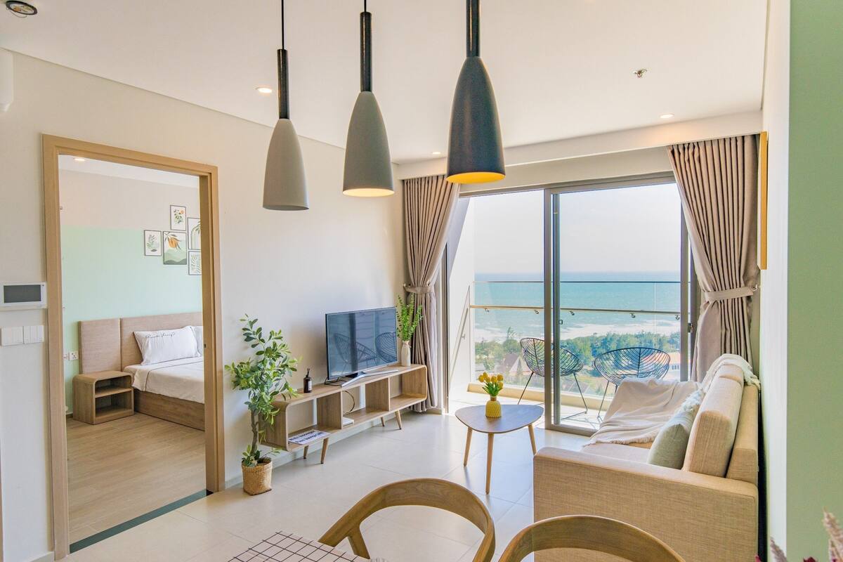 A modern living room with a sofa, TV, and dining area, featuring a large window with a city view.