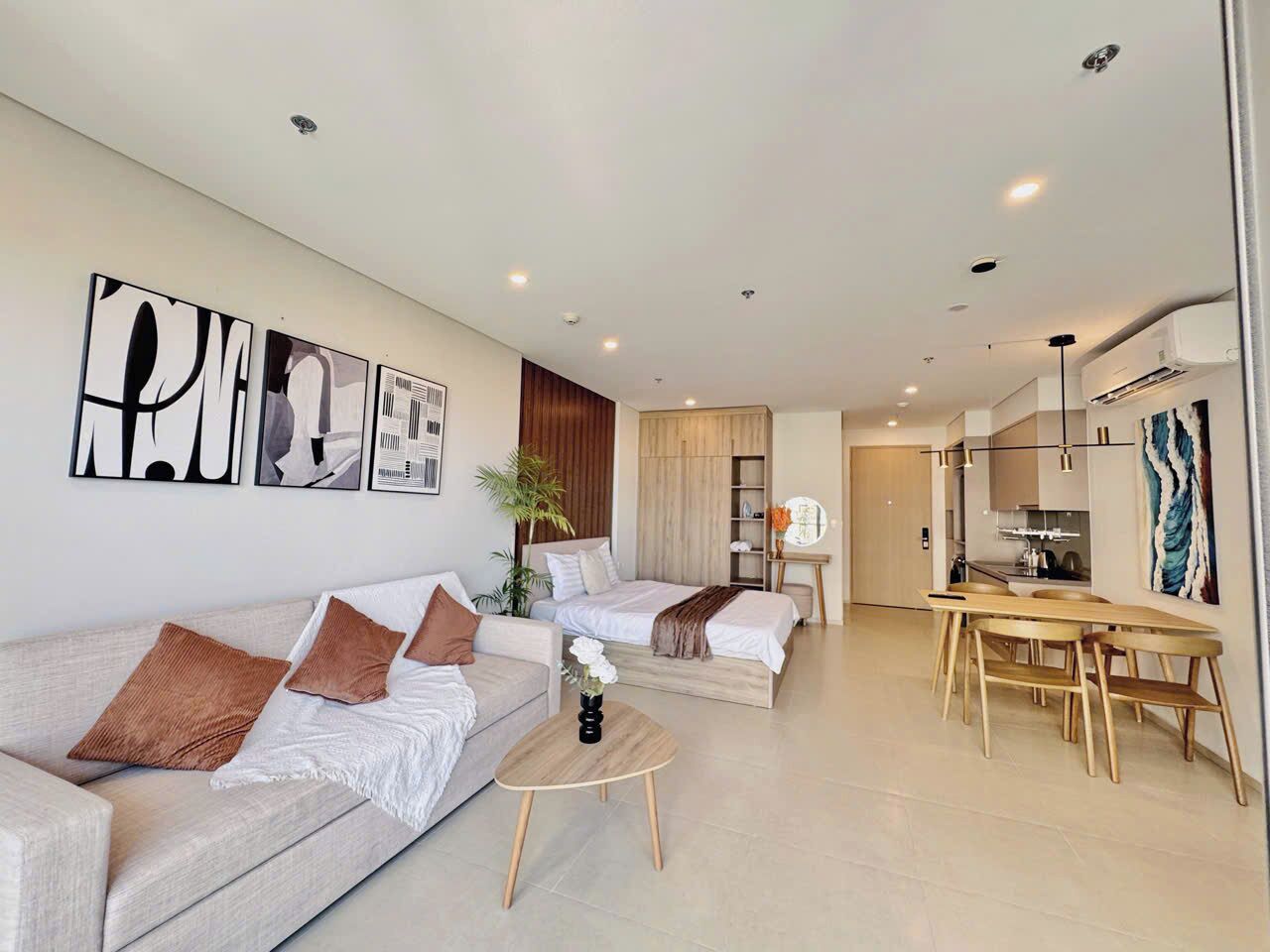 Una sala moderna con sofá, mesa de centro y cama con cabecera. Hay una zona de comedor con mesa y sillas.