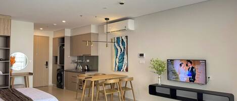 Una sala moderna con comedor, televisor montado en la pared y cocina al fondo.