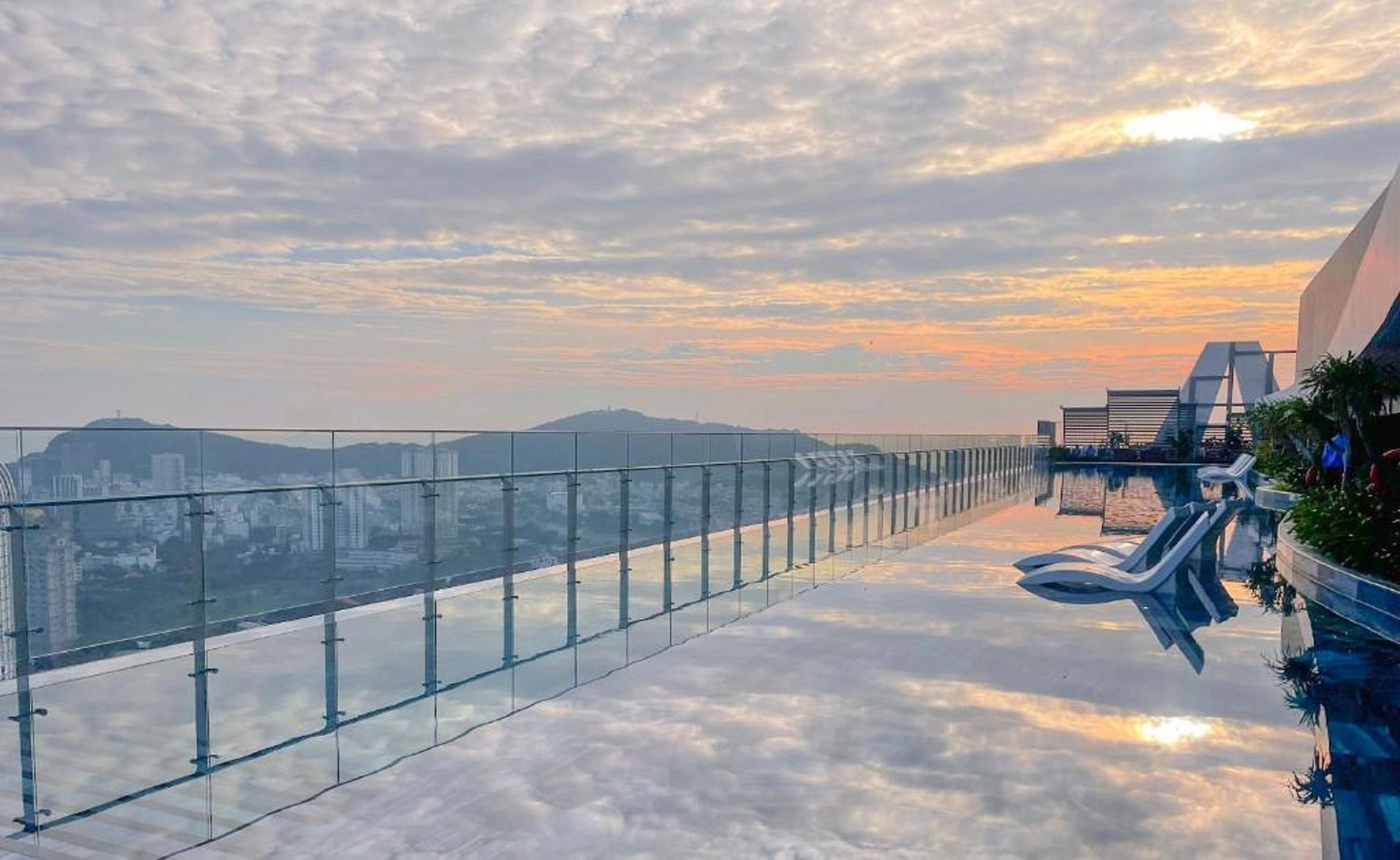 A glass-bottomed infinity pool with a cityscape view, modern architecture, and a clear sky.