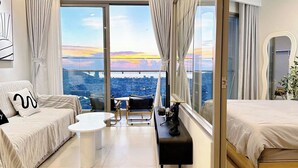 Una habitación de hotel moderna con balcón, un sofá, una cama, una mesita y una silla.