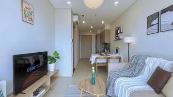 Un salon moderne avec un téléviseur à écran plat, un canapé, une table basse et un coin repas à l’arrière-plan.