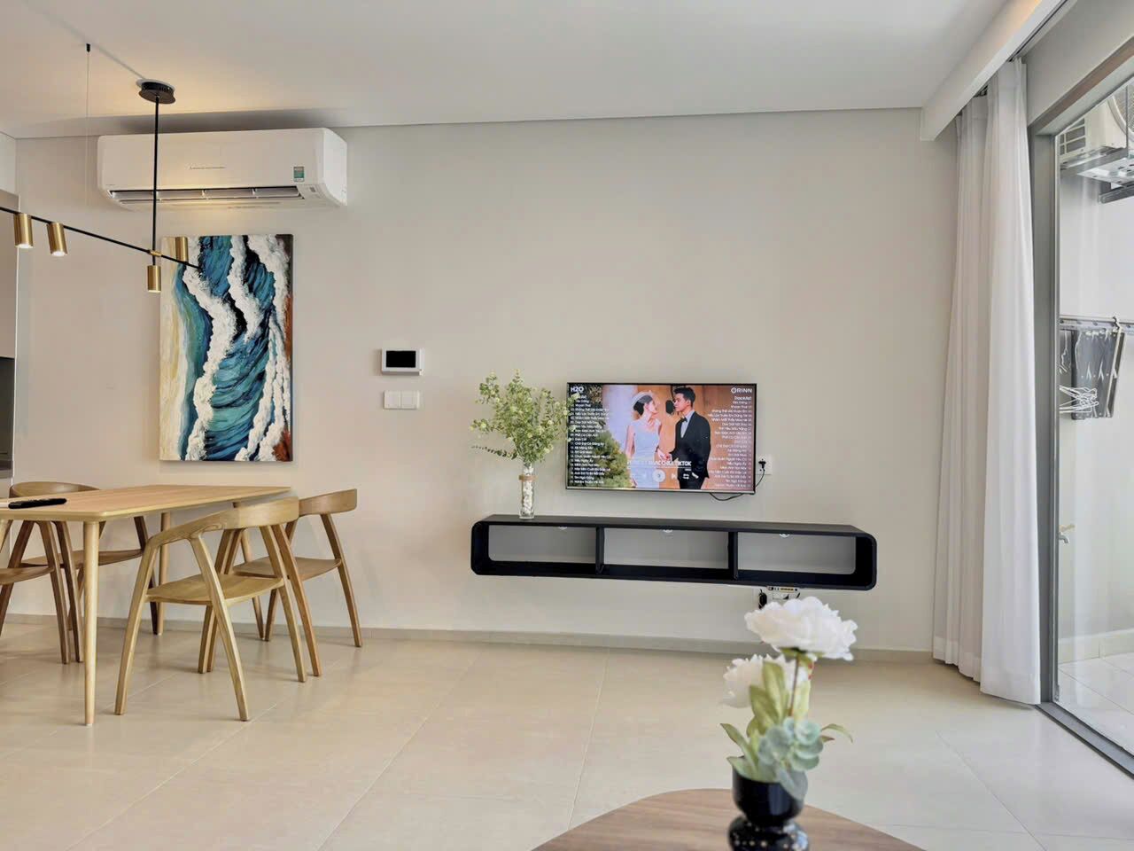 A modern living room with a dining area, a mounted TV, and a large window.