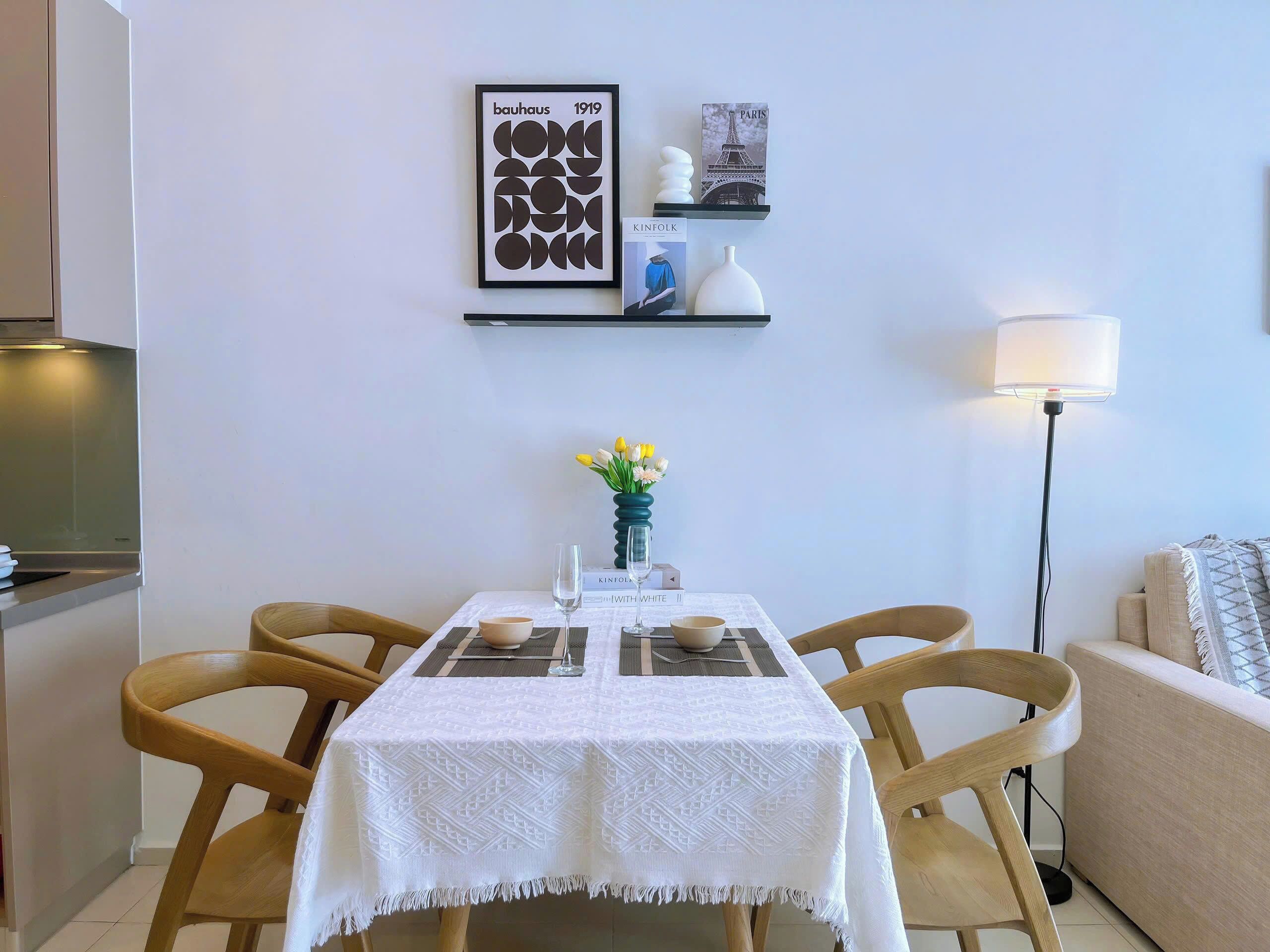 A dining area with a white table set for four, a vase of yellow flowers, and framed artwork on the wall.