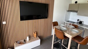 A modern kitchen with a built-in oven, a dining area with a table set for four, and a flat-screen TV mounted on the wall. - Seemingly cosy, close to the beach and in the heart of the golf course (Saint-Cyprien)