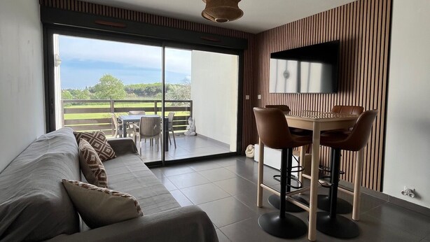 A modern bedroom with a large bed, a dining area with chairs, a TV mounted on the wall, and a sliding glass door leading to an outdoor patio. - Seemingly cosy, close to the beach and in the heart of the golf course (Saint-Cyprien)