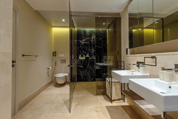 Une salle de bain moderne avec une douche à parois de verre, des toilettes et deux lavabos avec miroirs.
