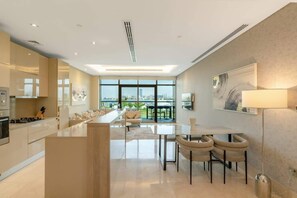 A modern kitchen with a central island, dining area with chairs, and a large window offering a city view.