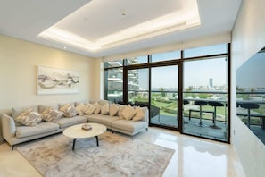A modern living room with a sectional sofa, a coffee table, and large floor-to-ceiling windows offering a city view.